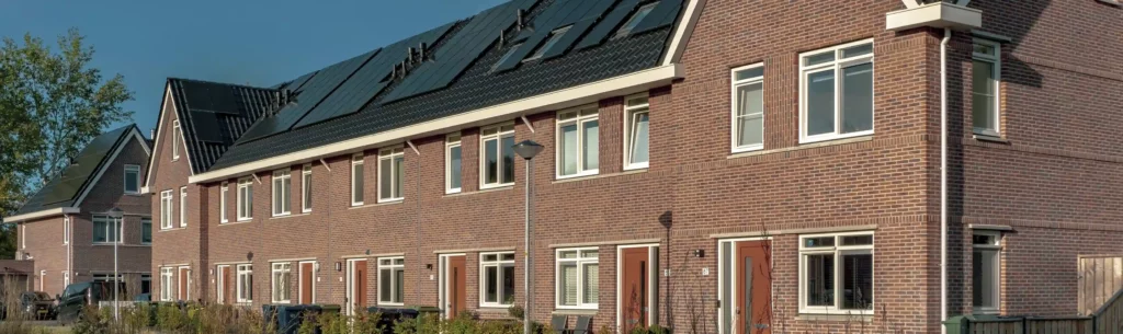 Rijtje nieuwbouwwoningen van een woningcorporatie met rode voordeuren en zonnepanelen op het dak.